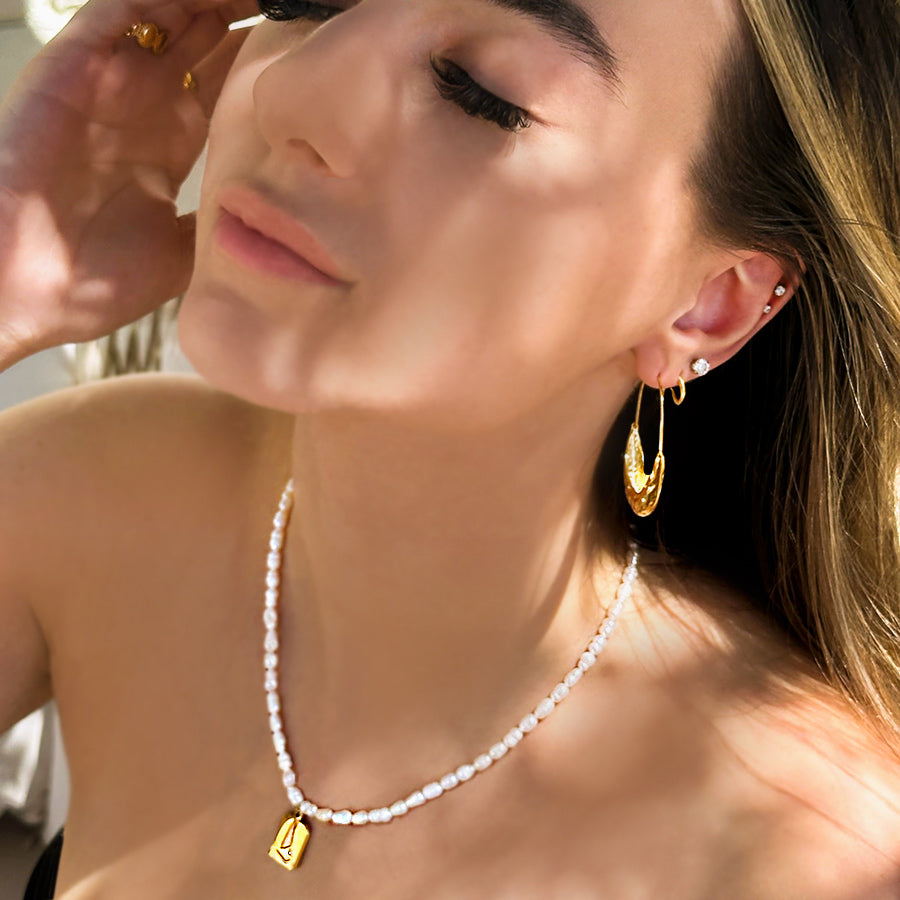 Girl wearing freshwater pearl beaded necklace with 18k gold plated pendant. Pendant is rectangular with abstract sailboat design with small cubic zirconia stone.