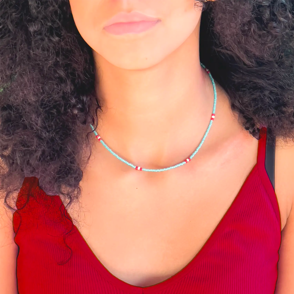 Girl wearing thin turquoise beaded necklace, red bead accents along chain. necklace paired with red tank.
