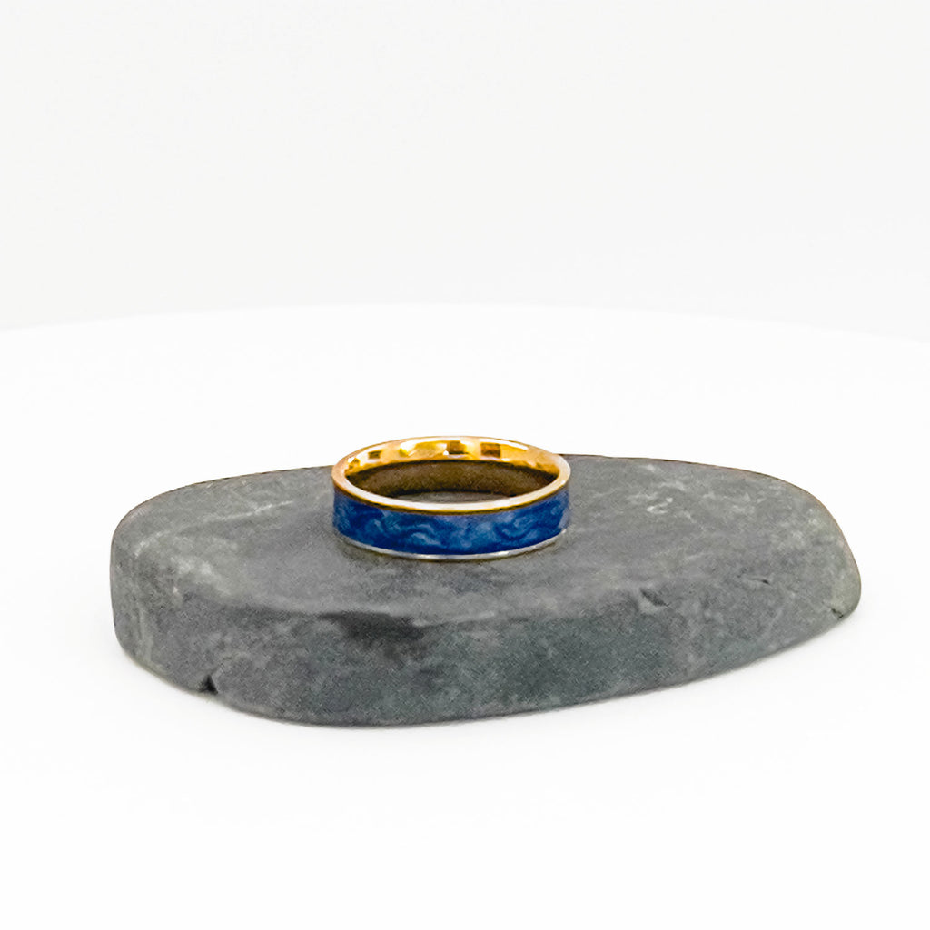 18k gold plated ring with a marbled blue enamel center, shown sitting on a rock.