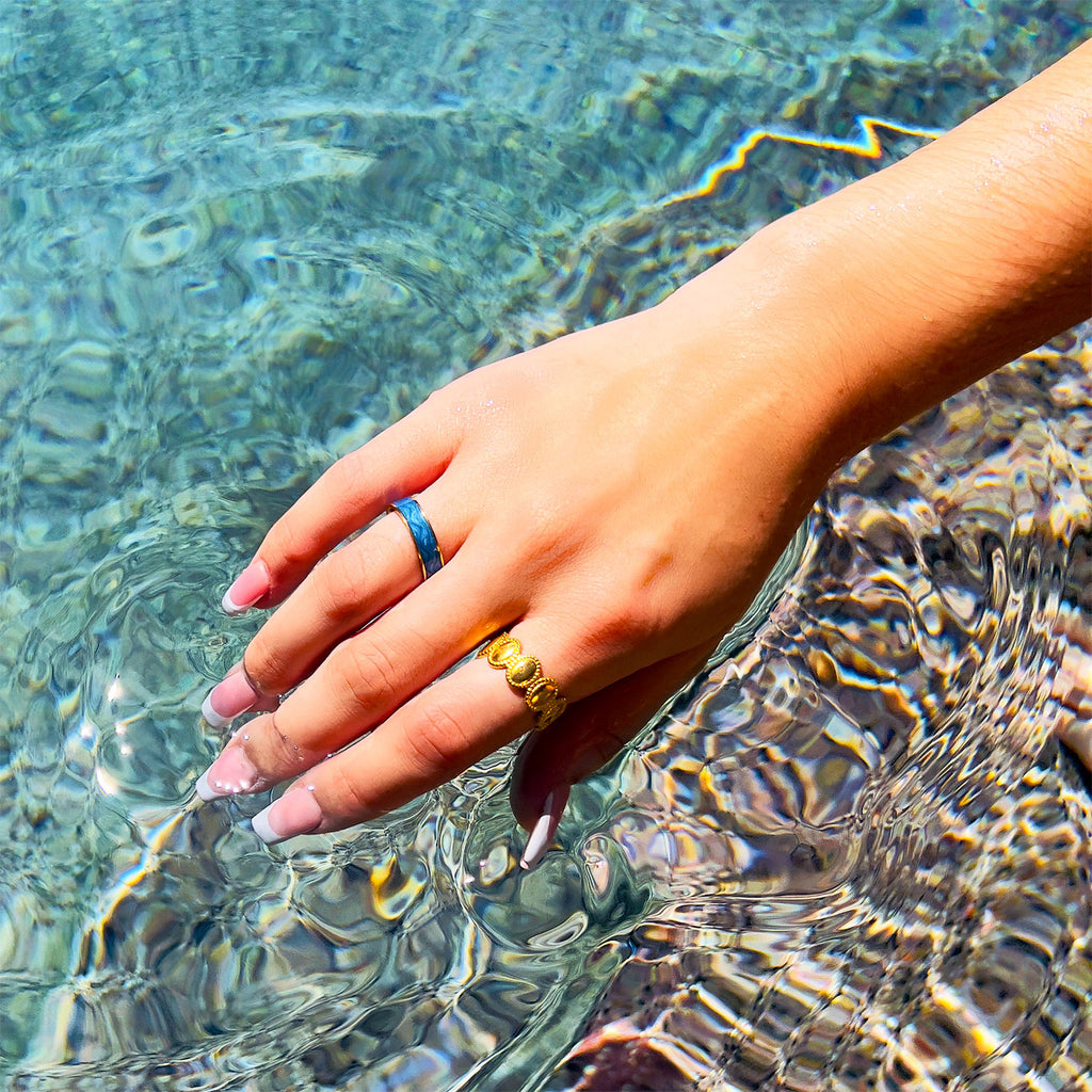 Girls hand over a pool of water with 18k gold plated ring with a marbled blue enamel center, paired with another gold-plated ring that is connected ovals design.