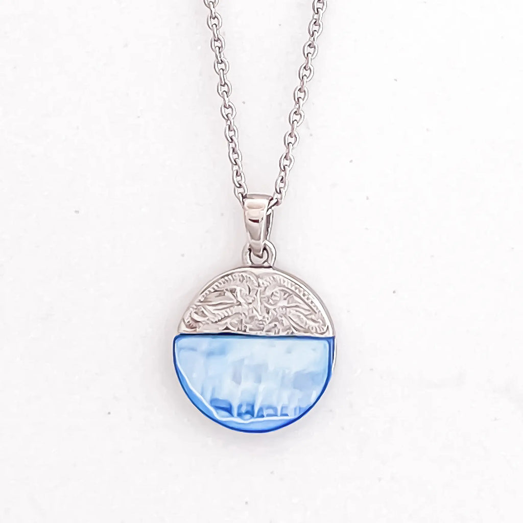 Silver color stainless steel pendant necklace, pendant is mixed media circle, top half is an engraved patterned silver and bottom half is a semi-transparent light blue natural shell stone.