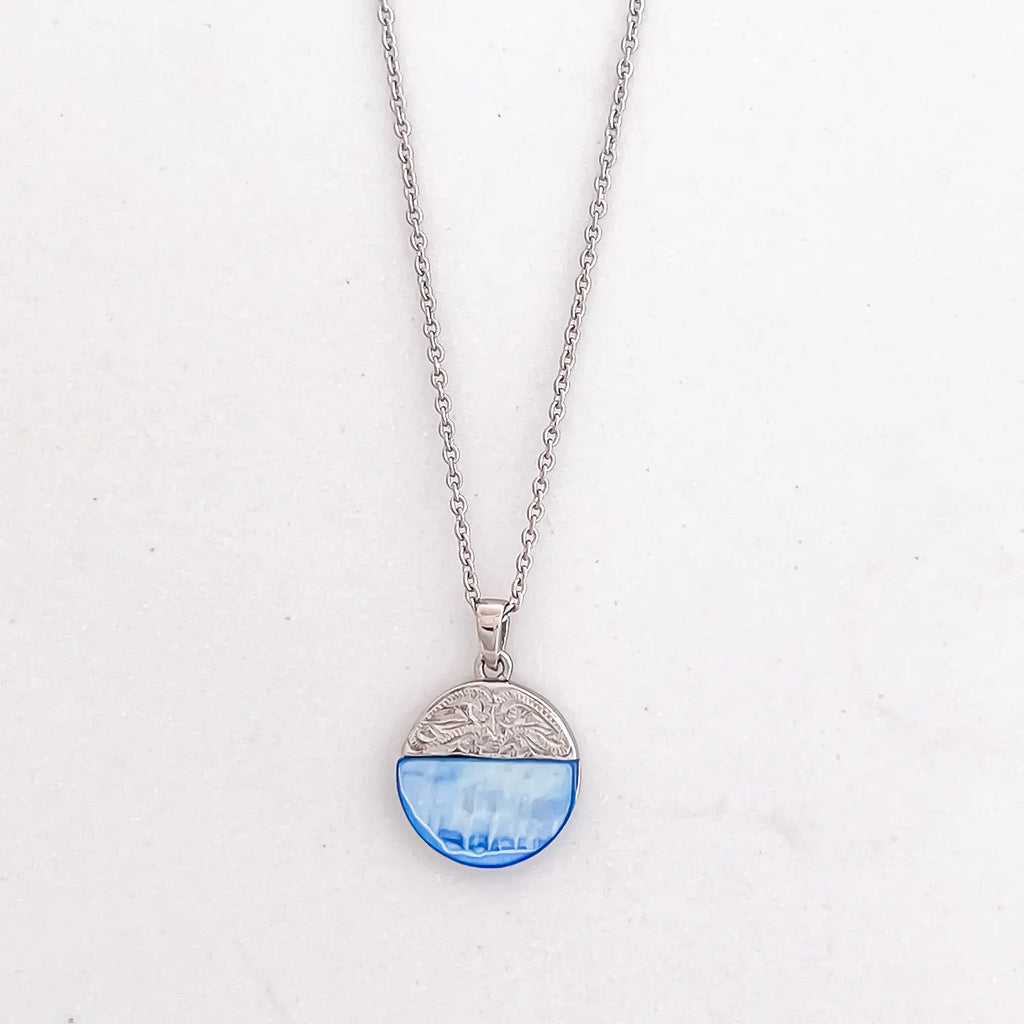 Silver color stainless steel pendant necklace, pendant is mixed media circle, top half is an engraved patterned silver and bottom half is a semi-transparent light blue natural shell stone.