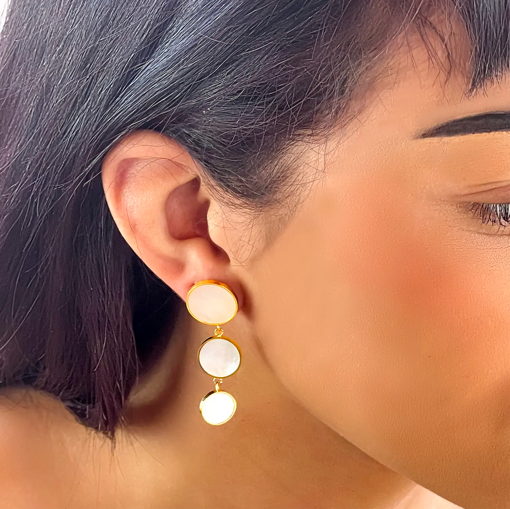 Girl wearing 18k gold-plated rimmed earrings around natural shell pastel color drop circles. Three circle sections, each circle gets smaller as it drops down.