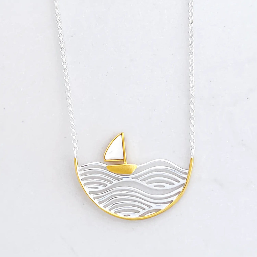 Sterling silver two-tone (silver and gold) sailboat pendant necklace, silver chain.  Pendant is a half circle. In the pendant is silver engraved waves, sitting on the wave is a small sail boat figure that is gold with a white sail. The rim of the half circle is also gold.