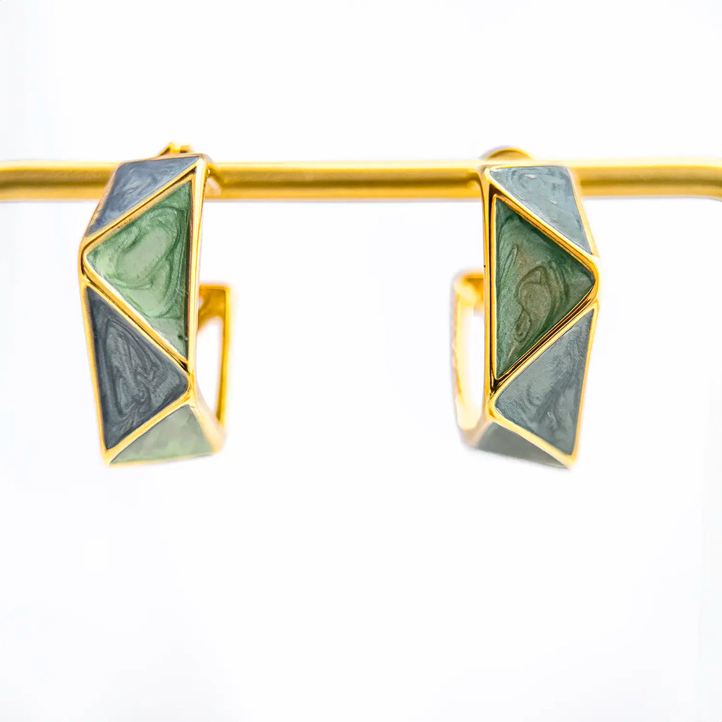 18k gold plated, geometric huggie earrings with blue/green enamel. Displayed on a stand.