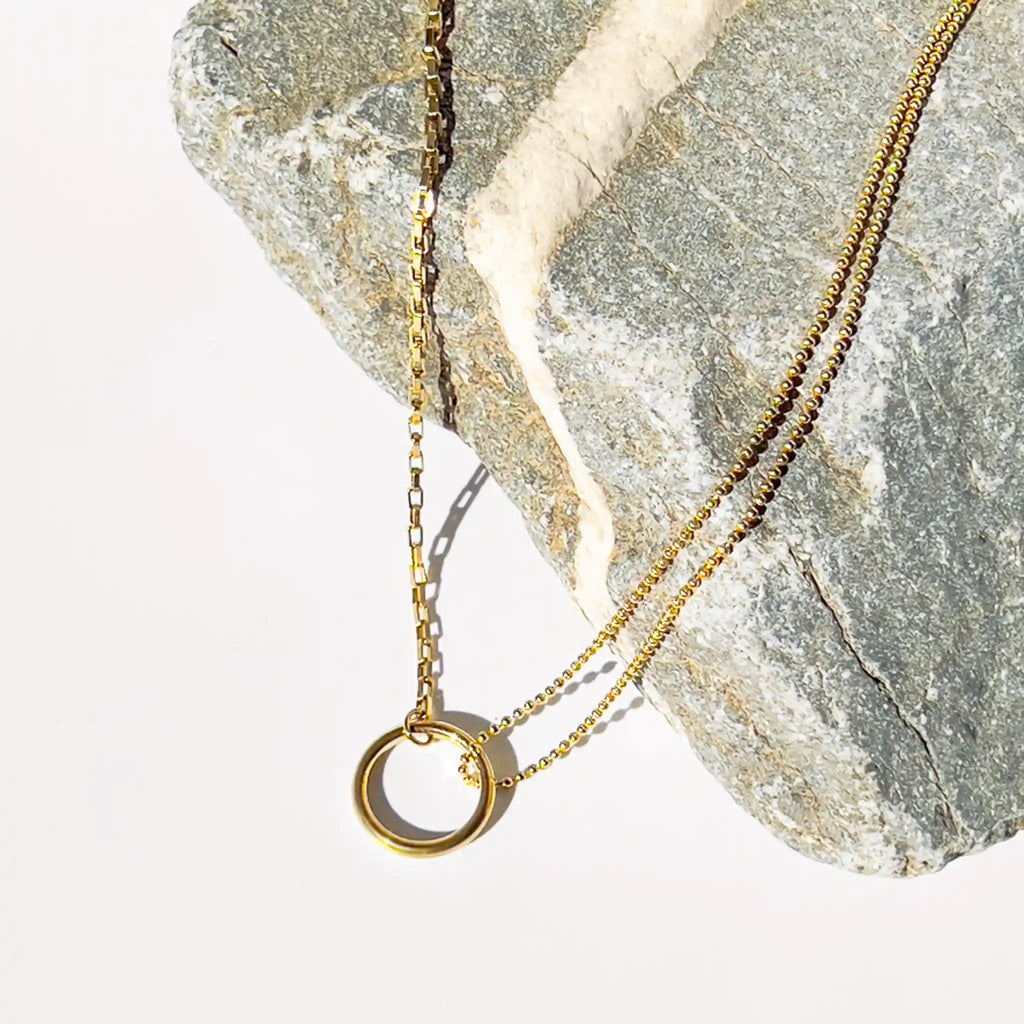 18k gold plated split chain necklace with "O" circle pendant connecting chains. One side of the chain is small circle beads and the other side is a typical chain-link style chain. Necklace shown displayed on a rock.