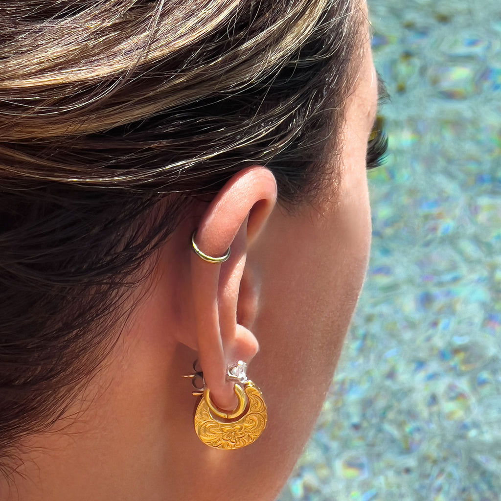Girl sitting by pool wearing 18k gold plated flower engraved small hoop earrings.
