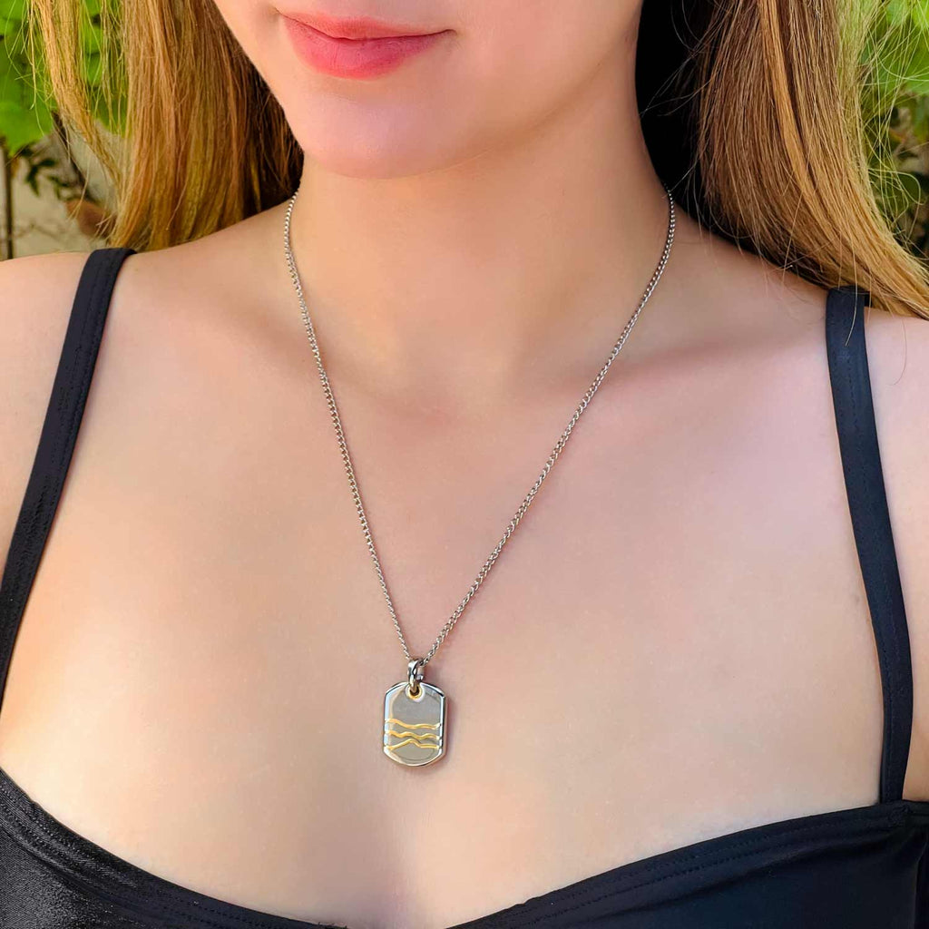Girl wearing Silver colored stainless steel dog-tag pendant necklace with 3 gold wave-like line accents on the pendant.