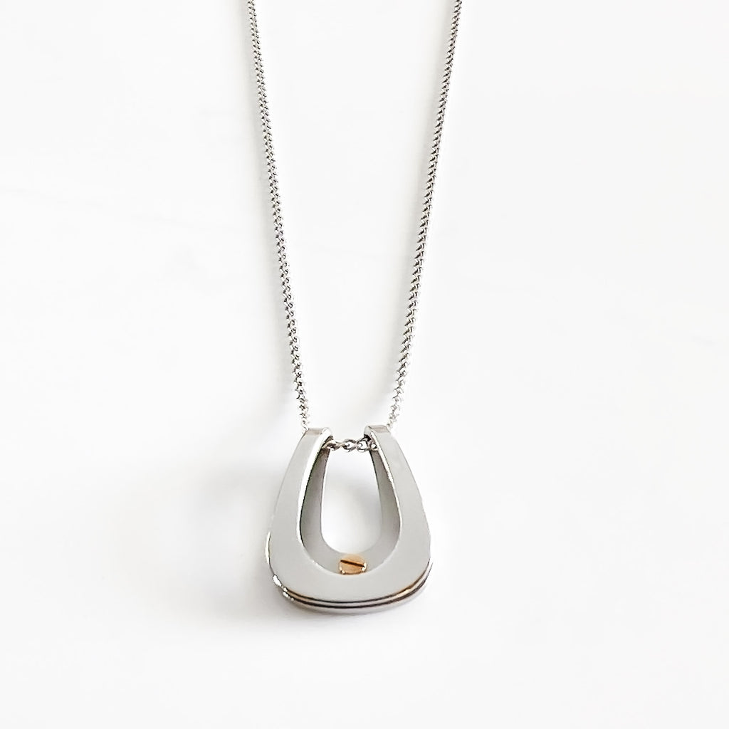 silver colored stainless steel horseshoe pendant necklace, with a small rose gold screw near the middle bottom of the horseshoe.