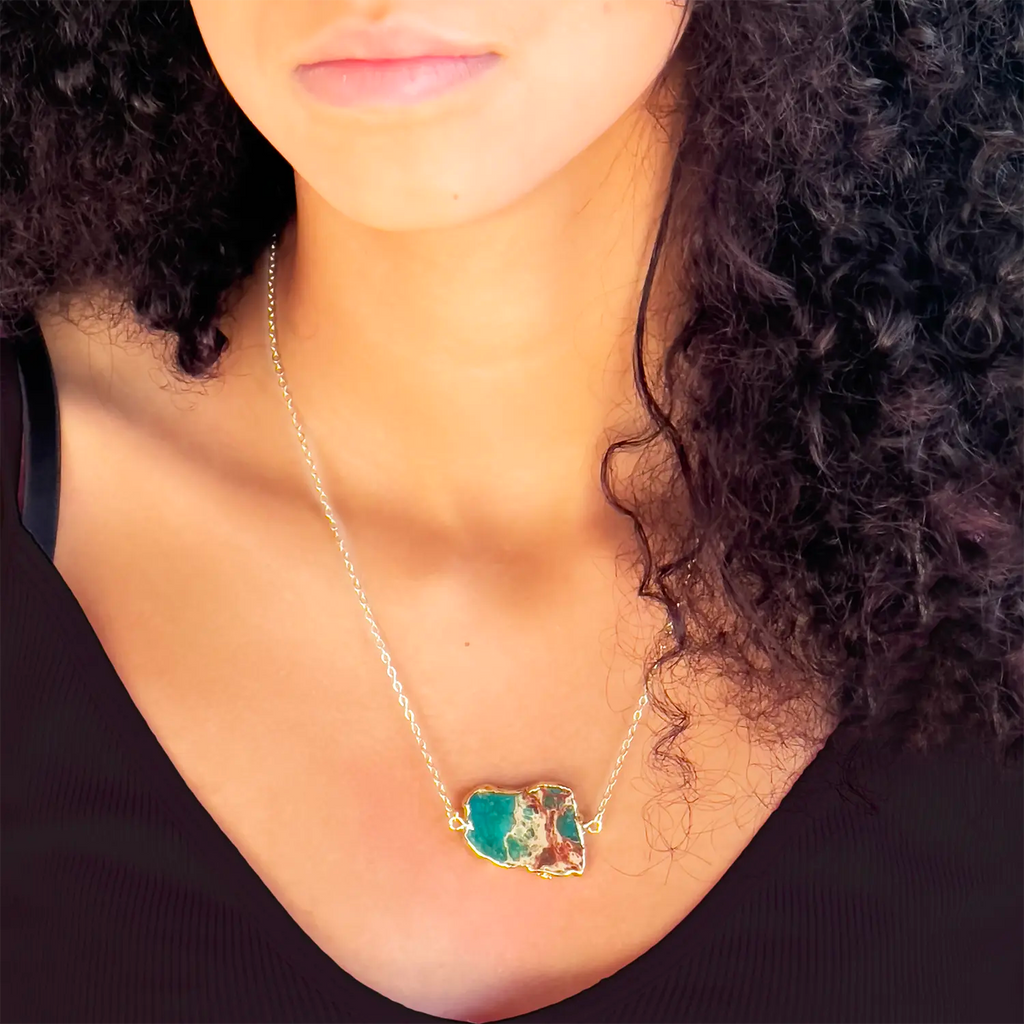 Girl wearing 18k gold plated pendant necklace, pendant is a turquoise stone with gold/yellow accent in the stone similar to ocean and land rock meeting.