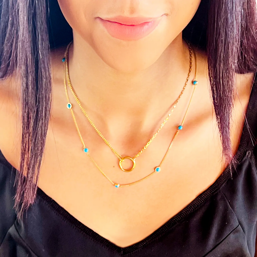 Girl wearing 18k gold plated split chain necklace with "O" circle pendant connecting chains. One side of the chain is small circle beads and the other side is a typical chain-link style chain. Necklace is layered with longer chain with evenly spaced out turquoise beads.