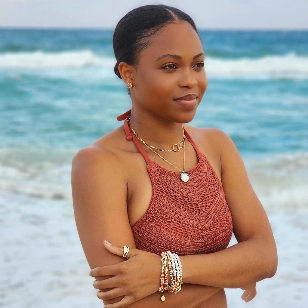 Girl standing by the ocean wearing 18k gold plated split chain necklace with "O" circle pendant connecting chains. One side of the chain is small circle beads and the other side is a typical chain-link style chain. Necklace is layered with a white circle pendant necklace.