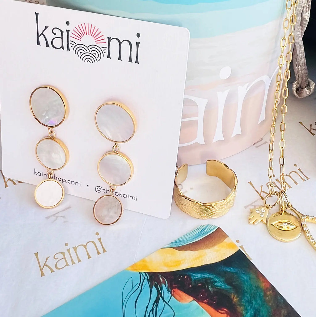 18k gold-plated rims around natural shell pastel color drop earrings. Three circle sections, each circle gets smaller as it drops down. These earrings in package shown with kaimi logo and gold-plated ring and charm necklace.