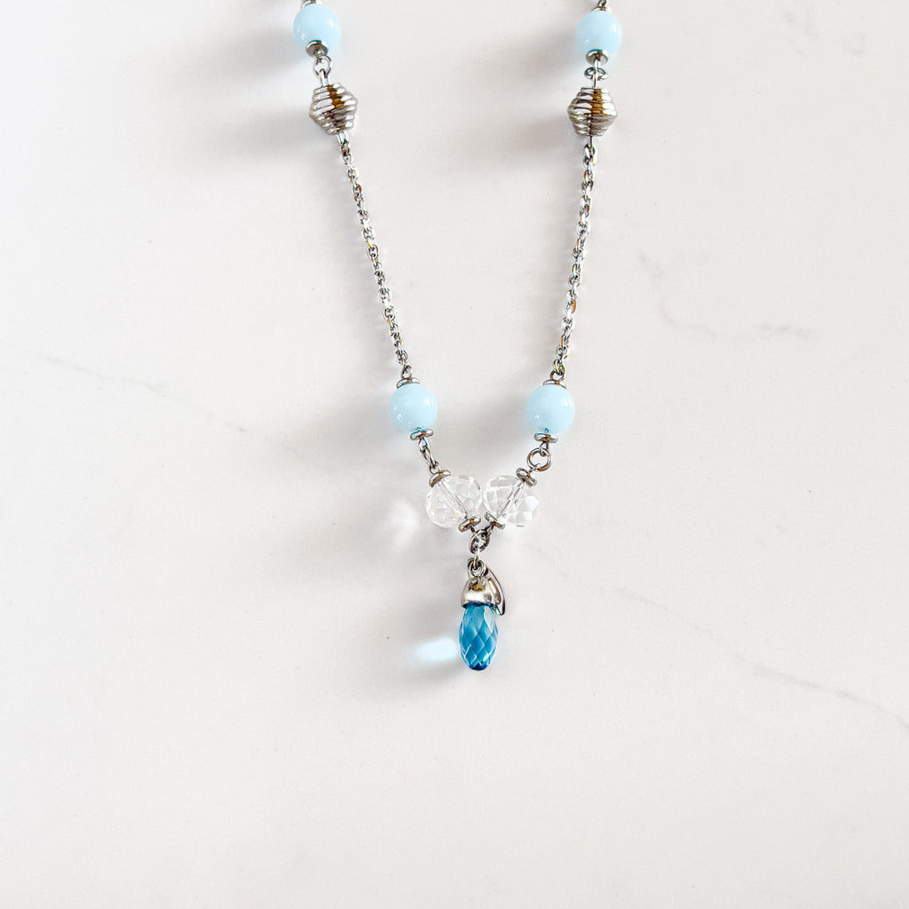 silver stainless steel chain necklace with two light blue beads, two clear stone beads, and an aqua pendant at the bottom. There is two more light blue circular beads closer to the top of necklace, and two silver beads directly under (one on each side)