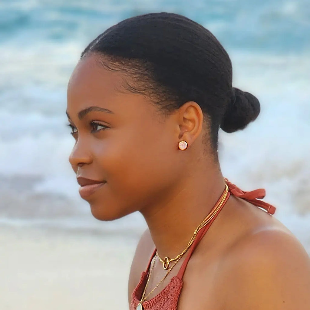 Girl by the beach wearing Druzy rose quartz stone stud earrings with 24k rose gold plated rims. Paired with two layered necklaces, both 18k gold plated chains with pendants. 
