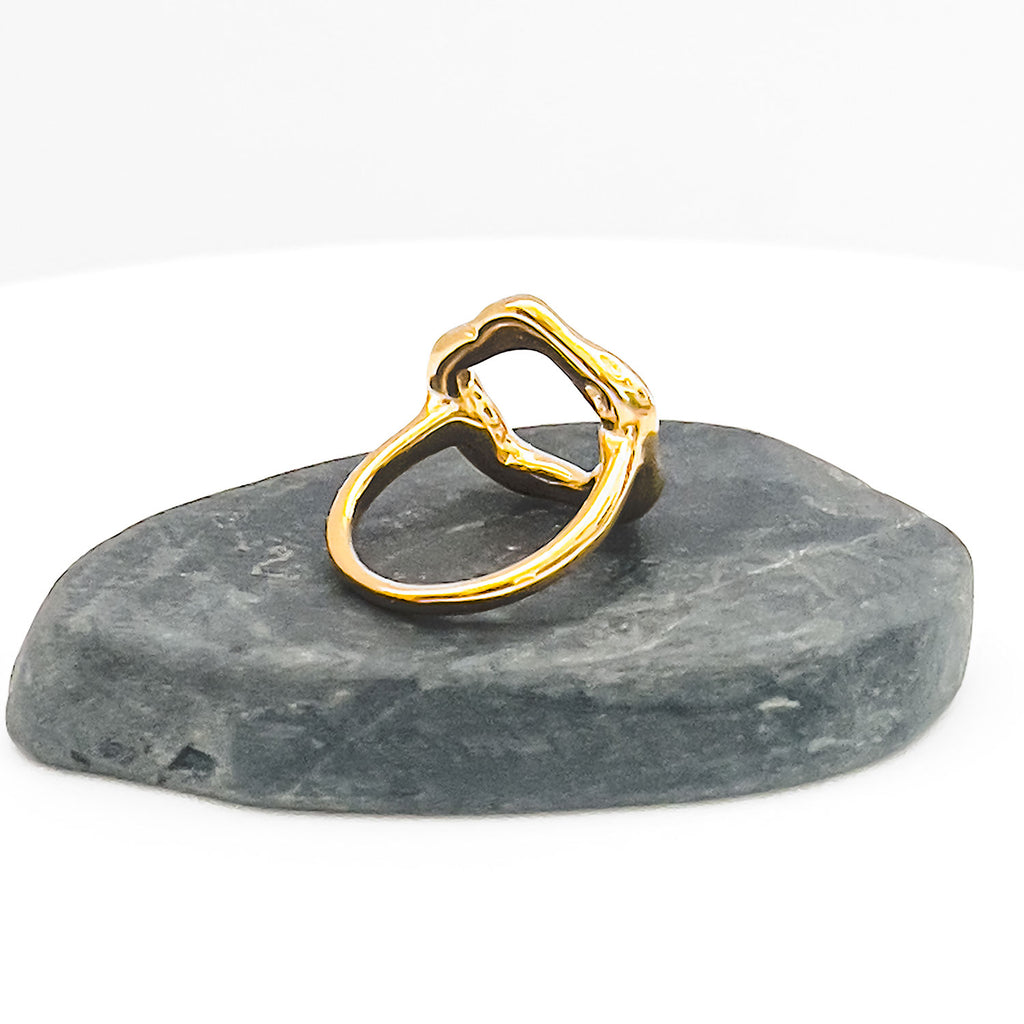18k gold plated ring with slightly mishapen circle. (abstract "O" on top) and displayed on a stone.