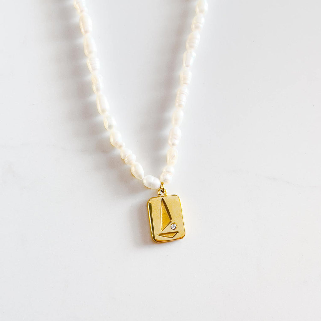 freshwater pearl beaded necklace with 18k gold plated pendant. Pendant is rectangular with abstract sailboat design with small cubic zirconia stone