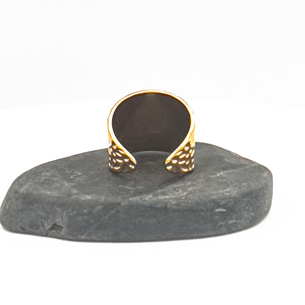 18k gold plated "hammered" adjustable ring, wide and plate with indented pattern. Displayed on a stone.