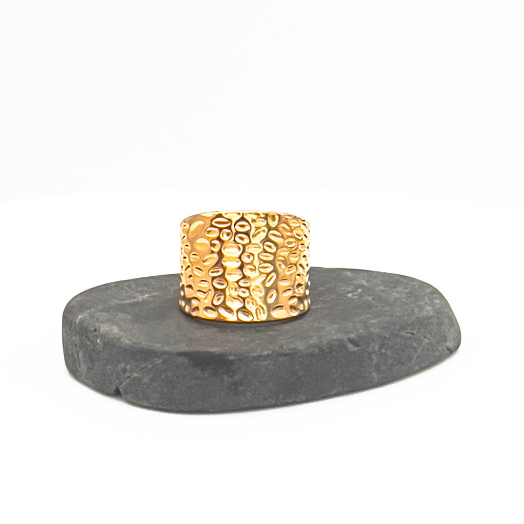 18k gold plated "hammered" adjustable ring, wide and plate with indented pattern. Displayed on a stone.