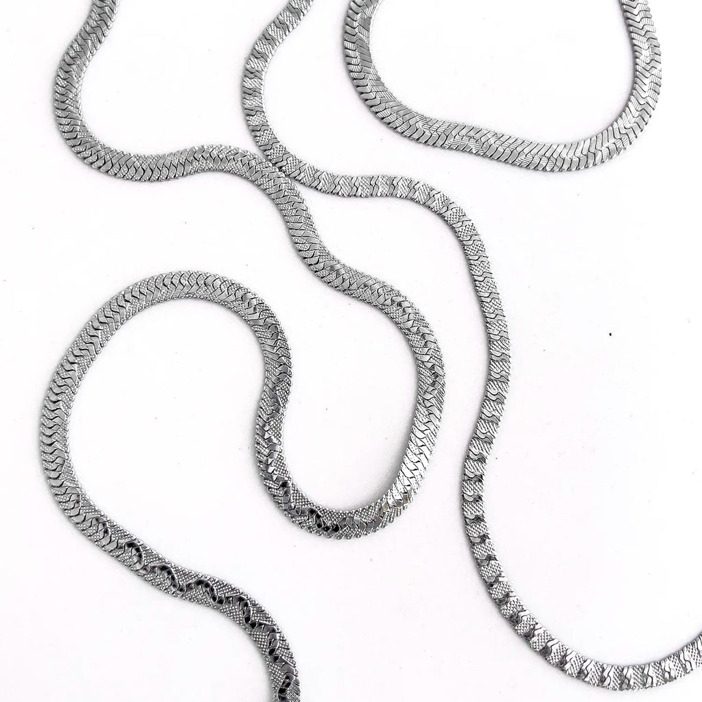 2 types of the silver color stainless steel textured snake chains laid down in a wiggly snake pattern. Both necklaces have different textured snake pattern.