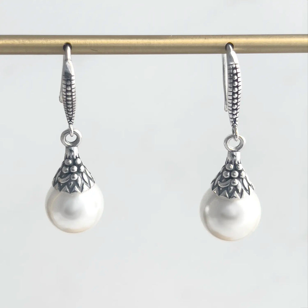 freshwater pearl and sterling silver drop earrings with a fishhook backing. Sterling silver has a pattern engraved. Earrings shown on a display.