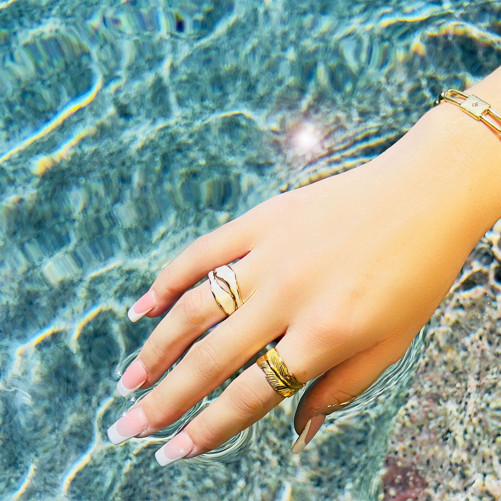 hand over pool wearing 18k gold plated enamel ring. Adjustable ring with wavy structure, color white.