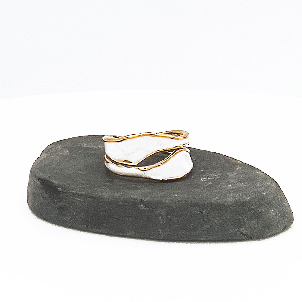18k gold plated enamel ring. Adjustable ring with wavy structure, color white. Displayed on a stone.
