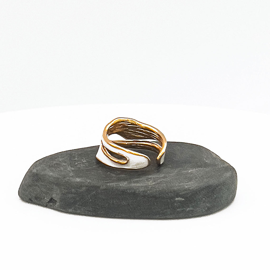 18k gold plated enamel ring. Adjustable ring with wavy structure, color white. Displayed on a stone.