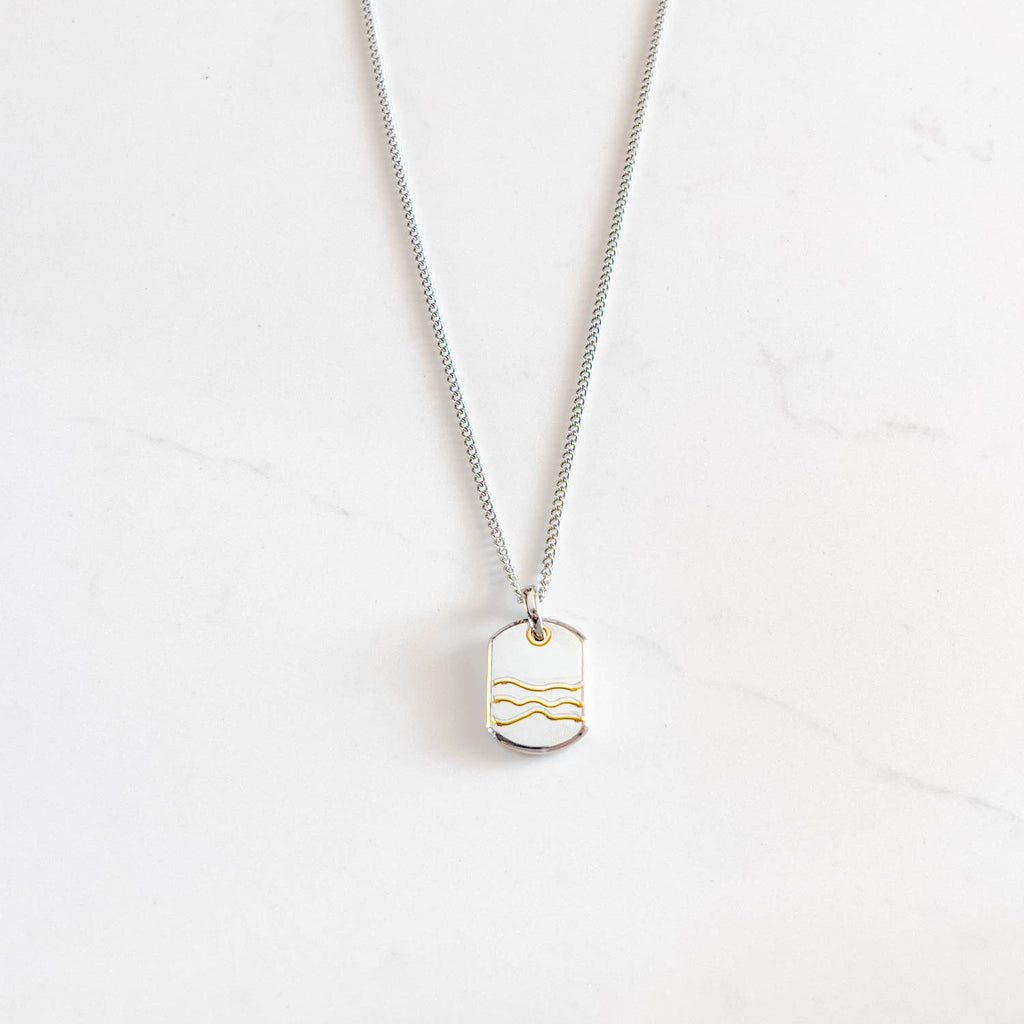 Silver colored stainless steel dog-tag pendant necklace with 3 gold wave-like line accents on the pendant.