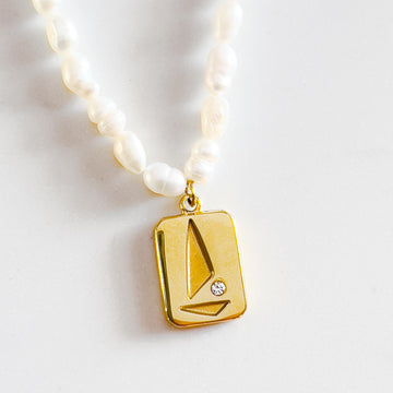 freshwater pearl beaded necklace with 18k gold plated pendant. Pendant is rectangular with abstract sailboat design with small cubic zirconia stone